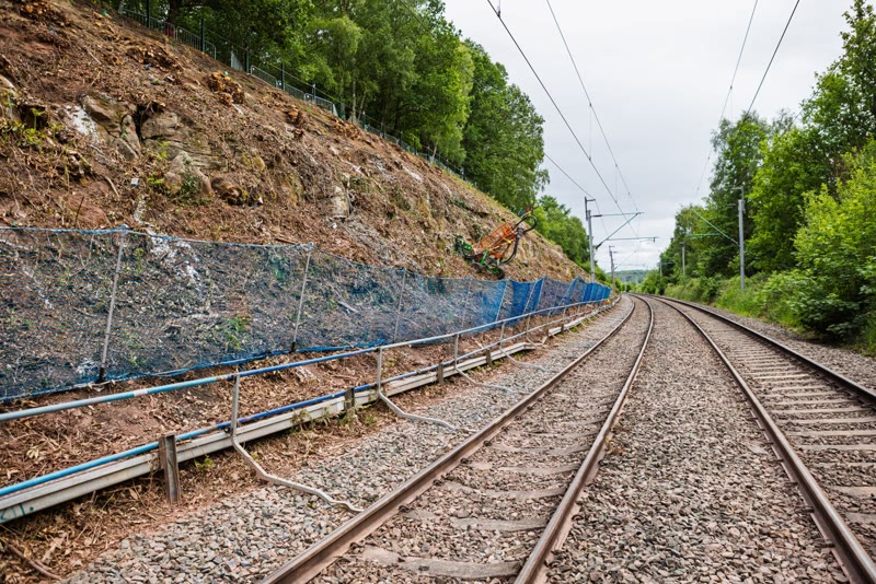 Rail embankment reinforced with mesh netting and rock armour
